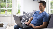 Yngre mand sidder i en sofa med sin laptop