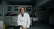 Billede af kvinde i hvid kittel, der sidder på en stol i et forskningslaboratorium
