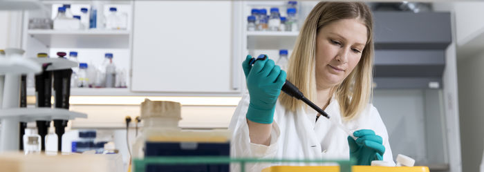 Ung forsker med grønne handsker arbejder koncentreret med celler i et glas